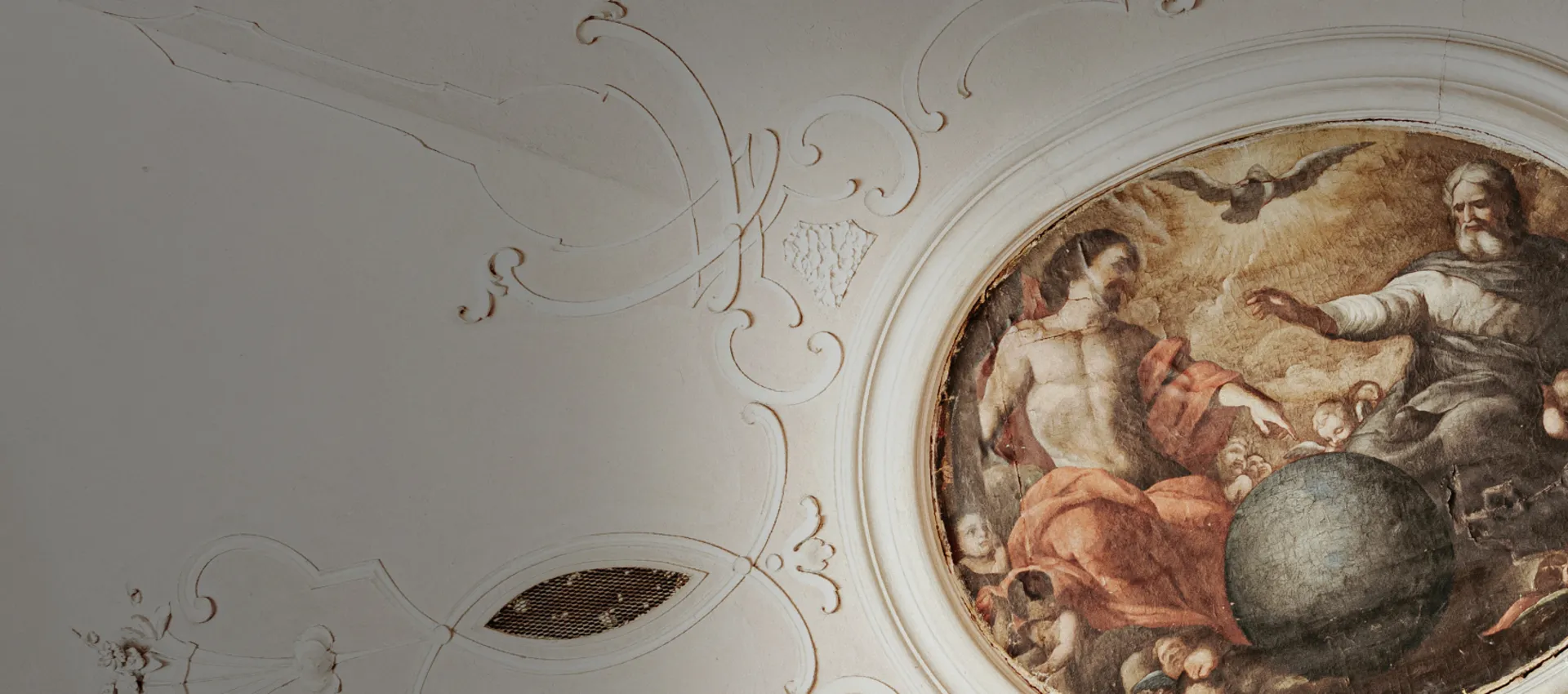 White ceiling facade with ornaments and a oval painting.